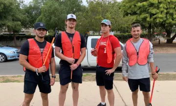 Four volunteers in orange vests participate in a community cleanup event.