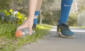 Photo of a person's feet and their hand picking up a plastic bottle from the ground and 
