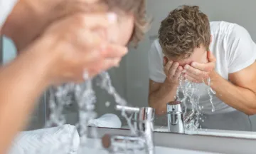 Man washing face in front of sink and mirror