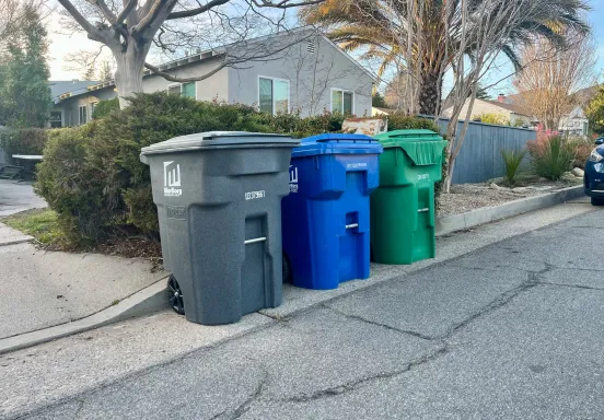 Gray (trash), blue (recycling), and green (yard waste) carts lined up on a street in Santa Barbara