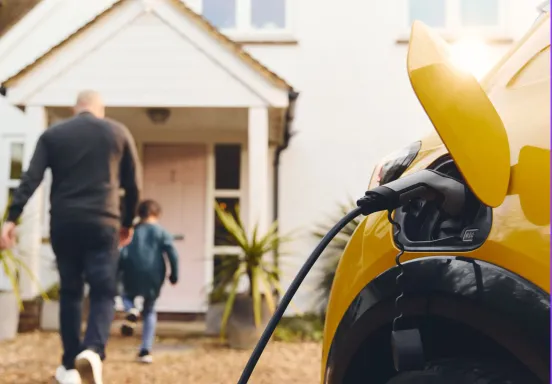 Yellow electric vehicle charging as family walk into a house in the background