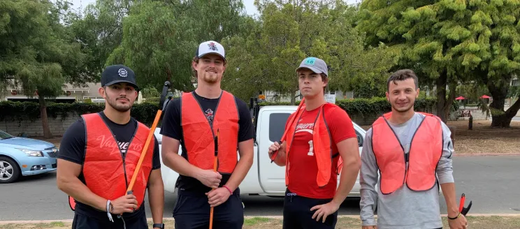 Four volunteers in orange vests participate in a community cleanup event.