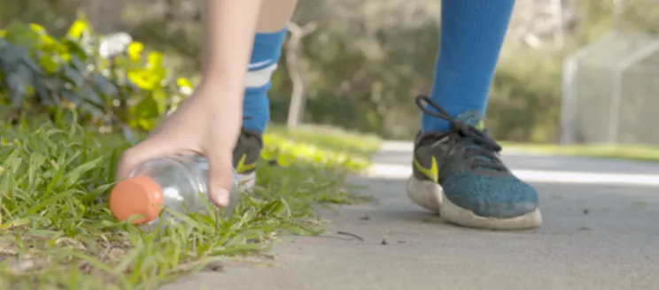 Photo of a person's feet and their hand picking up a plastic bottle from the ground and 