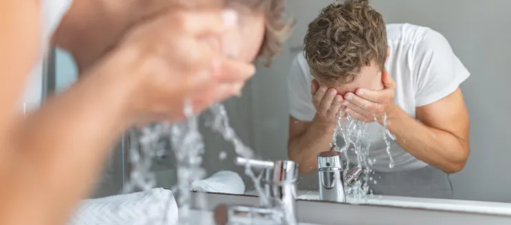 Man washing face in front of sink and mirror