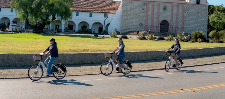 Three people riding BCycles in front of Old Mission Santa Barbara