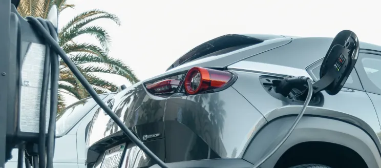 Stock image of grey electric vehicle plugged in to charge