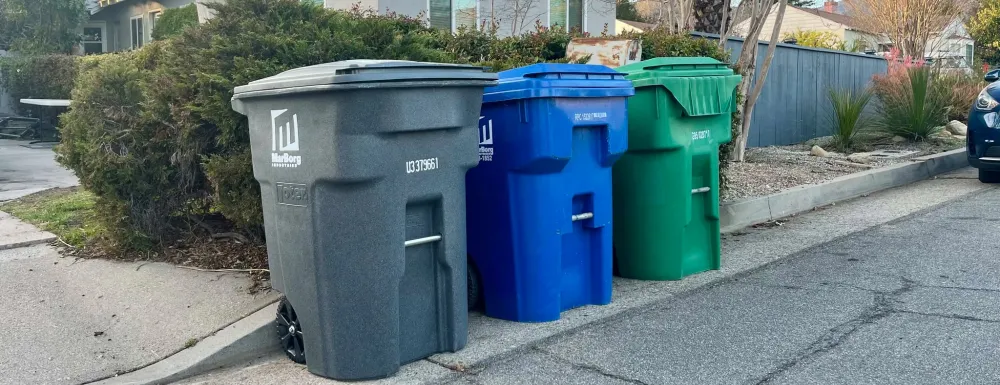 Gray (trash), blue (recycling), and green (yard waste) carts lined up on a street in Santa Barbara