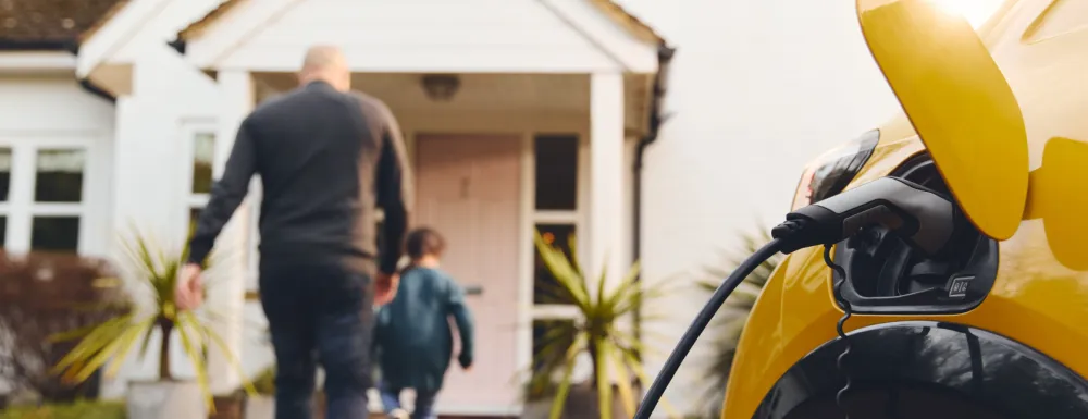 Stock image of an electric vehicle charging as family walks into home in the background