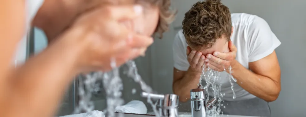 Stock image of a man washing his face in a bathroom sink at mirror