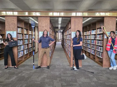 4 people stand in the book stacks holding tools that can be found in the library's Tool Library collection